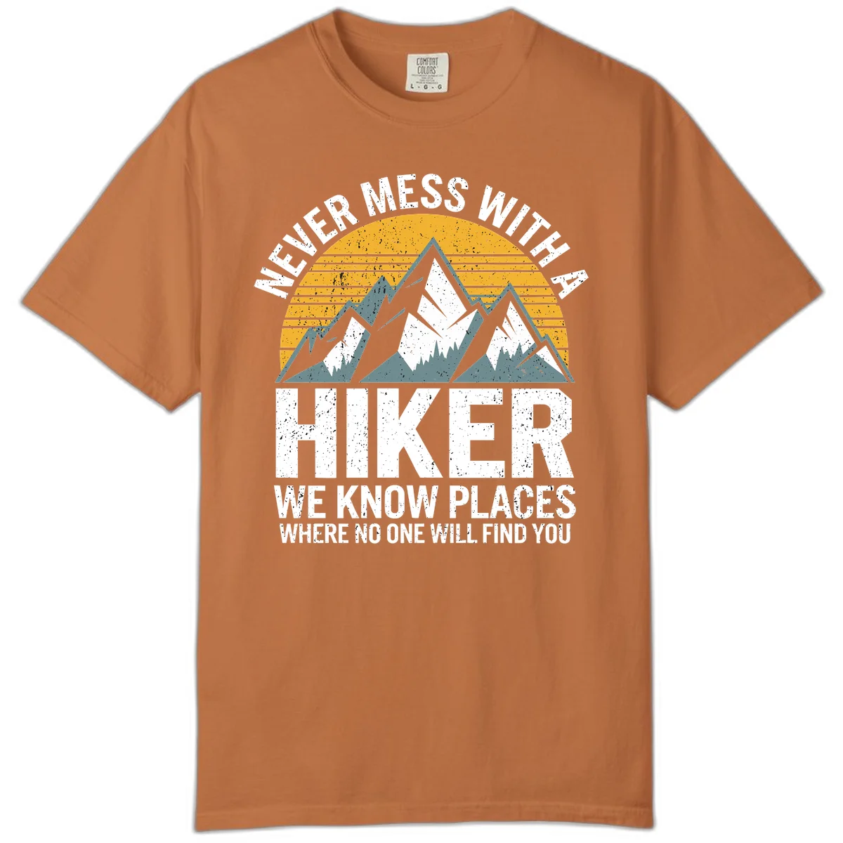 Vintage-style design with snow-capped mountains and forest silhouette against striped sunset, text reads 'Never Mess With A Hiker We Know Places Where No One Will Find You' in Yam