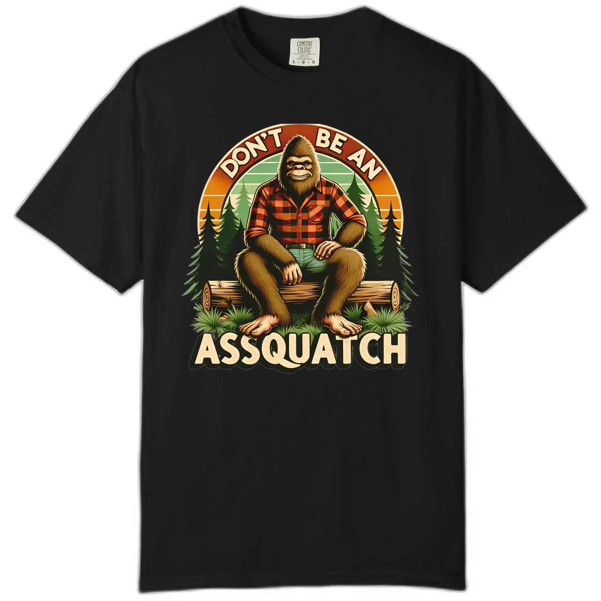 Vintage badge design with friendly Bigfoot in plaid shirt sitting on a log with forest trees, text reads 'Don't Be An Assquatch' in Black
