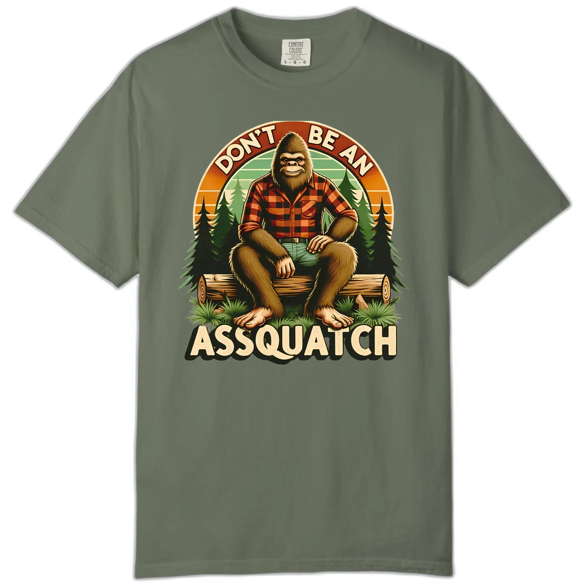 Vintage badge design with friendly Bigfoot in plaid shirt sitting on a log with forest trees, text reads 'Don't Be An Assquatch' in Moss