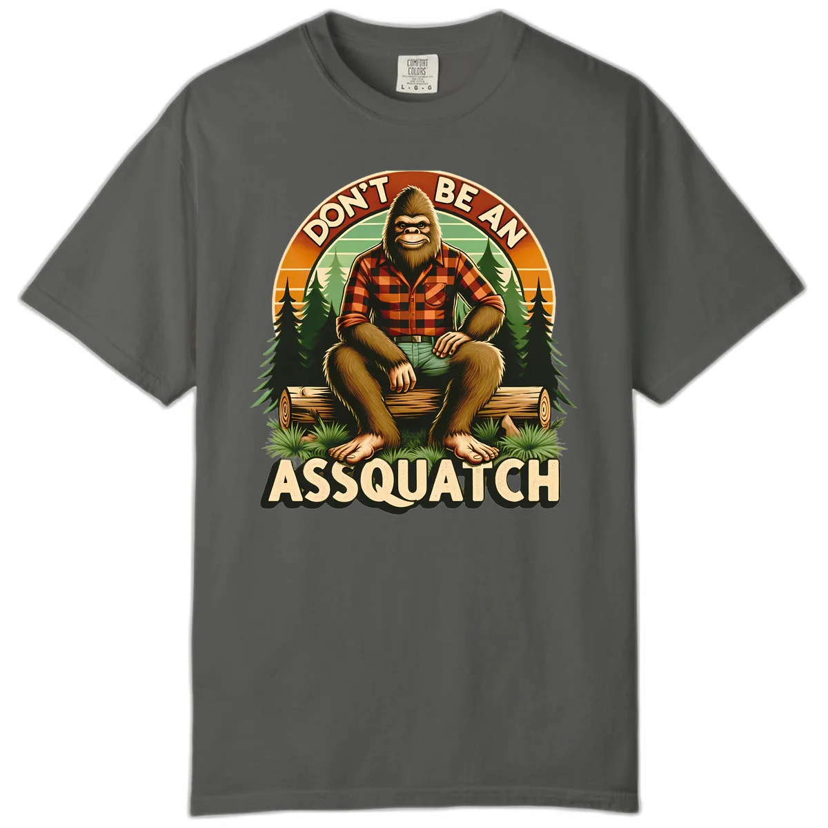 Vintage badge design with friendly Bigfoot in plaid shirt sitting on a log with forest trees, text reads 'Don't Be An Assquatch' in Pepper