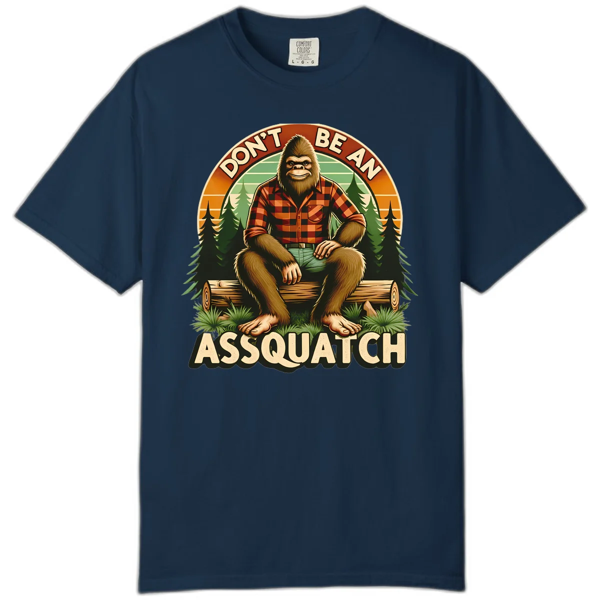 Vintage badge design with friendly Bigfoot in plaid shirt sitting on a log with forest trees, text reads 'Don't Be An Assquatch' in True Navy