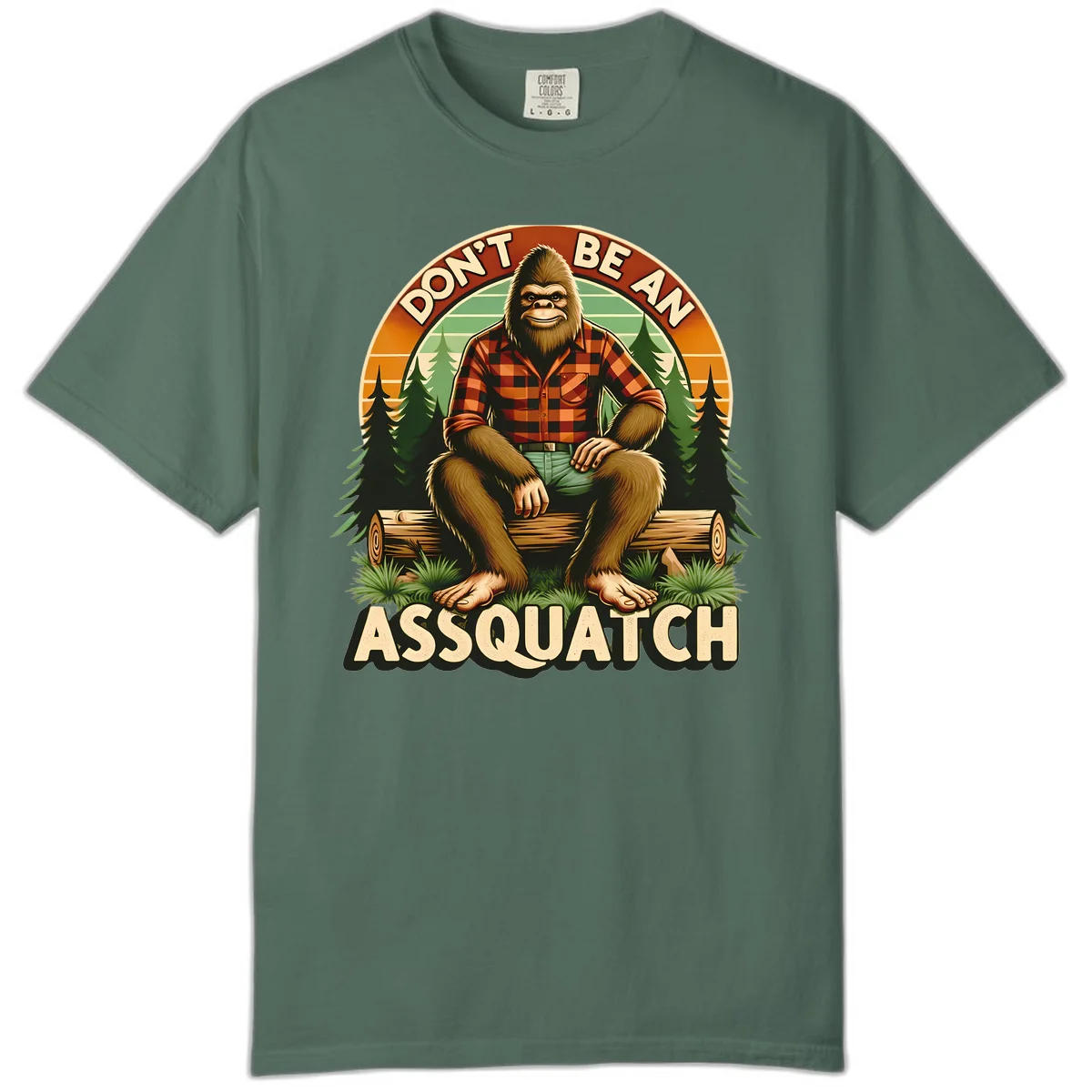 Vintage badge design with friendly Bigfoot in plaid shirt sitting on a log with forest trees, text reads 'Don't Be An Assquatch' in Blue Spruce