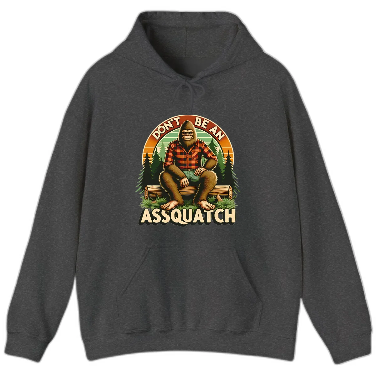 Vintage badge design with friendly Bigfoot in plaid shirt sitting on a log with forest trees, text reads 'Don't Be An Assquatch' in Dark Heather